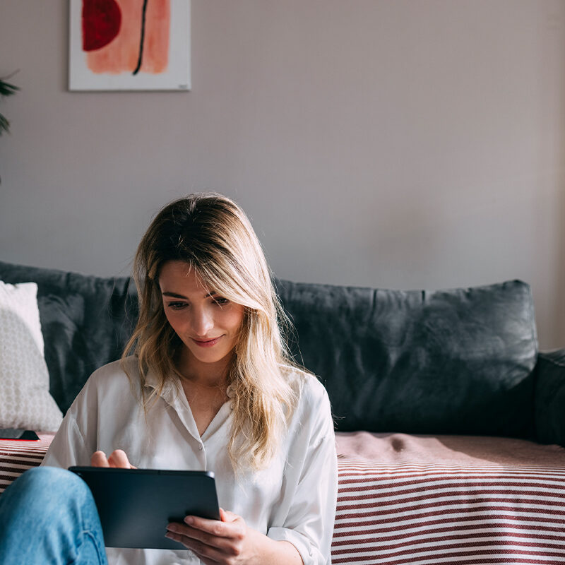 A woman sitting in her home looks at a tablet, and enjoys her beautiful complexion after laser skin resurfacing in Davis County