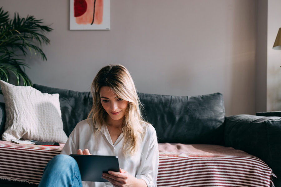 A woman sitting in her home looks at a tablet, and enjoys her beautiful complexion after laser skin resurfacing in Davis County